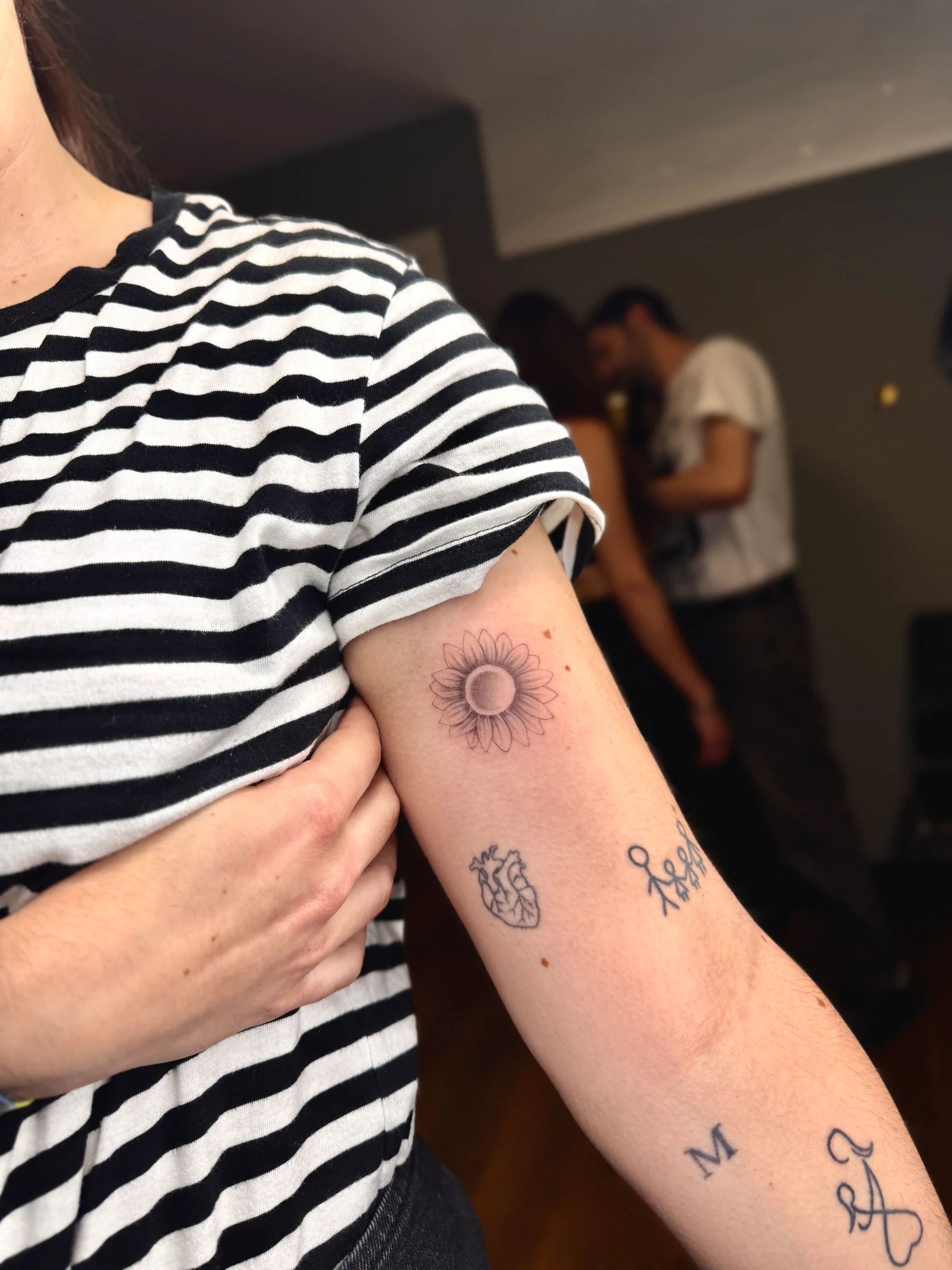 Varios tatuajes pequeños en el brazo: un sol, un corazón y letras